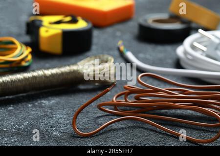 Verschiedene elektrische Kabel und Werkzeuge auf schwarzem, strukturiertem Tisch, Nahaufnahme Stockfoto