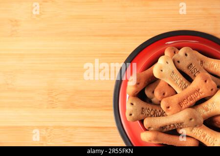 Knochenförmige Hundekekse in der Fütterschüssel auf dem Holztisch, Draufsicht. Platz für Text Stockfoto