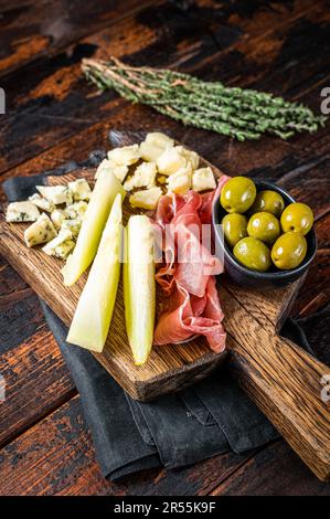 Käse- und Fleischplatte, Antipasti mit Prosciutto-Schinken, Parmesan, Blauschimmelkäse, Melone und Oliven auf Holzbrett. Holzhintergrund. Draufsicht. Stockfoto