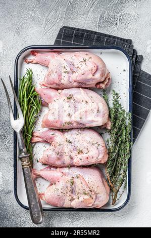 Rohes Wachtelfleisch mit Gewürzen, Knoblauch und Kräutern, fertig zum Kochen in Backform. Weißer Hintergrund. Draufsicht. Stockfoto