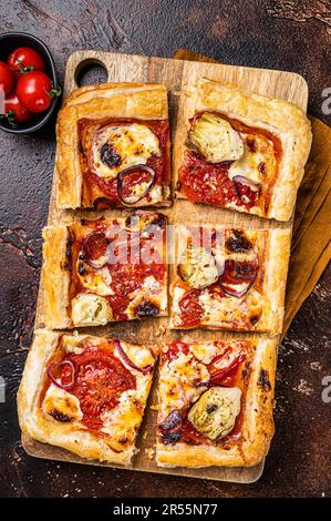 Vegetarische Blätterteigpizza mit Artischocke, Mozzarella, Tomaten und Käse auf einem Holzbrett. Dunkler Hintergrund. Draufsicht. Stockfoto