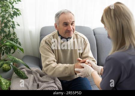 Fürsorgliche Krankenschwester spricht mit altem Patienten hält seine Hand sitzen im Wohnzimmer bei Homecare Besuch bieten psychologische Unterstützung zuhören klagt Empathie zeigen Stockfoto
