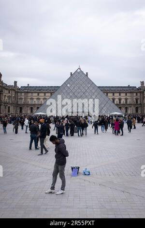 Die berühmte Louvre-Pyramide und das elegante Palais Royale stehen an einem ruhigen grauen Frühlingstag in Paris, Frankreich, Seite an Seite. Inmitten einer belebten Menschenmenge von Besuchern und Touristen verbinden diese architektonischen Meisterwerke Modernität und Geschichte und laden zu Entdeckungen und Wertschätzung ein. Erleben Sie die harmonische Mischung aus Alt und Neu, während das reiche kulturelle Erbe der Stadt inmitten der pulsierenden Energie eines beliebten Reiseziels zum Leben erwacht. Stockfoto