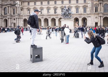 Touristen machen Fotos vor der Pyramide des Lovre im Innenhof des eleganten Palais Royale, die an einem ruhigen grauen Frühlingstag in Paris auf den Eintritt in das Kunstmuseum des Louvre warten. Inmitten einer belebten Menschenmenge von Besuchern und Touristen verbinden diese architektonischen Meisterwerke Modernität und Geschichte und laden zu Entdeckungen und Wertschätzung ein. Erleben Sie die harmonische Mischung aus Alt und Neu, während das reiche kulturelle Erbe der Stadt inmitten der pulsierenden Energie eines beliebten Reiseziels zum Leben erwacht. Stockfoto