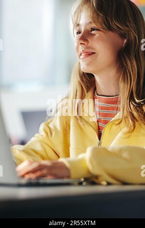 Glückliches junges Mädchen, das auf eine digitale Lesekompetenz mit einem Lächeln im Gesicht achtet. Sie sitzt an ihrem Schreibtisch mit einem Laptop und will unbedingt lernen und Stockfoto