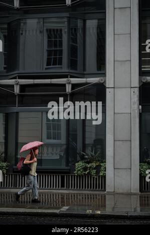 London, Vereinigtes Königreich: Eine Frau läuft im Regen eine Straße entlang und trägt einen Regenschirm. Alte Broad Street in der City of London. Stockfoto