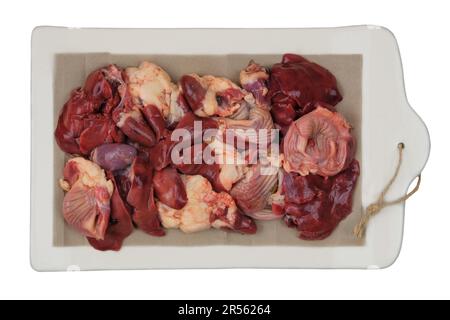 Rohe Hühnchen-Innereien auf einer Keramikplatte isoliert auf weißem Hintergrund. Hühnermagen, -Herzen und -Lebern werden zum Kochen zubereitet. Stockfoto