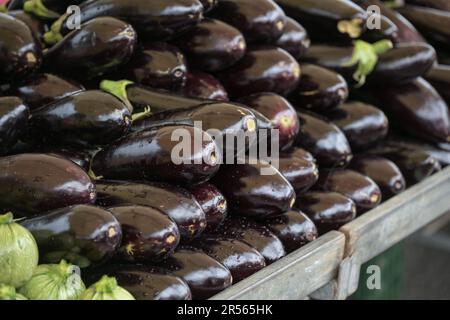 Frische und glänzende Auberginen, die sich auf einem Marktstand stapeln, pflanzliche Zutaten für mediterrane Gerichte, ausgewählter Fokus, schmale Feldtiefe Stockfoto