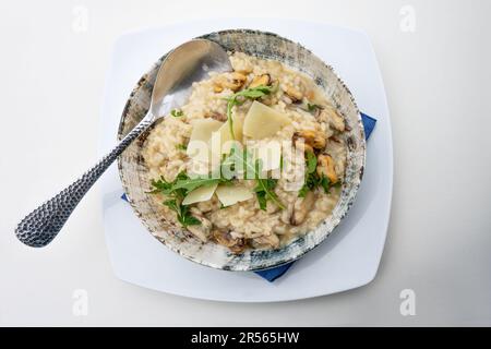 Risotto mit Muscheln, Rucola und Parmesankäse, mediterrane Mahlzeit serviert auf einem rustikalen Keramikteller, Blick von oben, Kopierbereich, Auswahl Stockfoto