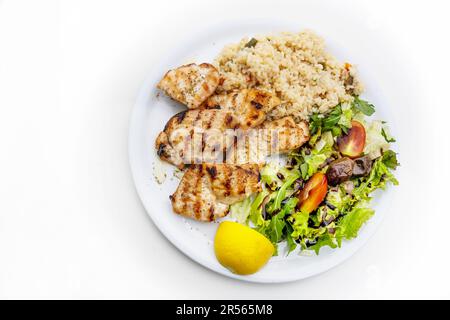 Gegrilltes Hähnchenfilet mit gemischtem Salat, Reis und Zitrone, mediterranes Gericht serviert auf einem Teller, weißer Tisch, Kopierraum, Blick von oben, se Stockfoto