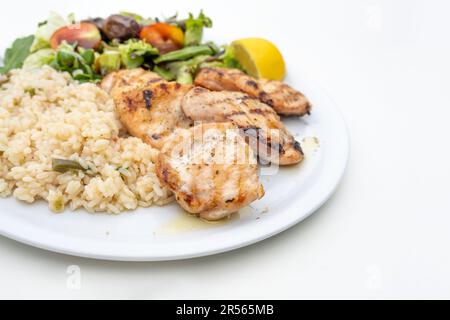 Gebratenes Hähnchenfilet mit Reis, gemischtem Salat und Zitrone, mediterrane Mahlzeit serviert auf einem Teller, weißer Tisch, Kopierraum, ausgewählter Fokus, enge Tiefe o Stockfoto