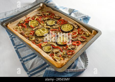 Ofengemüse mit Kräutern und Gewürzen auf einem Backblech auf einem blauen Küchentuch und einem weißen Tisch, mediterranes vegetarisches Essen, Kopierraum, SE Stockfoto