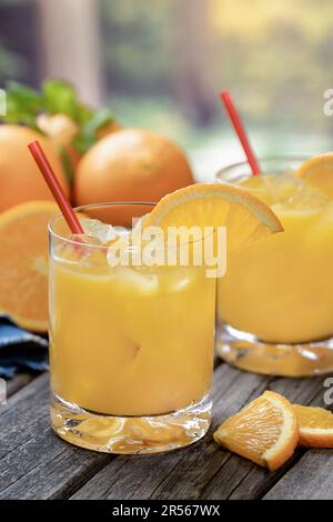 Orangensaftcocktail mit Orangenscheiben und frischen Orangen auf einem alten Holztisch mit Naturkulisse Stockfoto