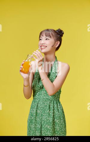 Lächelnde junge Frau vor der gelben Wand, die Orangensaft trinkt Stockfoto