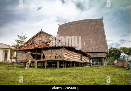 Hinter einem traditionellen „nha rong“, oder Kulturhaus, mit seinem segelähnlichen Strohdach, das der ethnischen Minderheit der Bahnar nebenan gehört Stockfoto