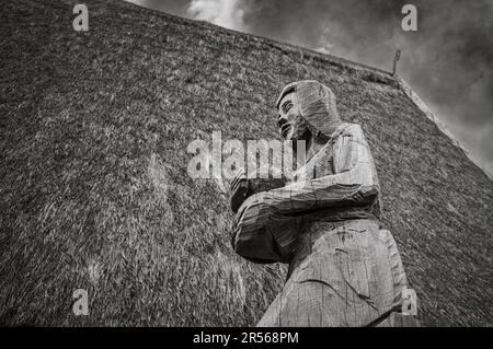 Ein Schnitzerei einer knienden Frau mit einem Riesenkopf steht Wache am Eingang eines traditionellen „nha rong“, oder Kulturhauses, das der Bahnar Ethnic gehört Stockfoto
