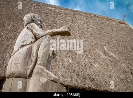 Die Schnitzerei eines Mannes steht bewacht am Eingang eines traditionellen „nha rong“, oder Kulturhauses, das der ethnischen Minderheit der Bahnar in Kon XOML gehört Stockfoto