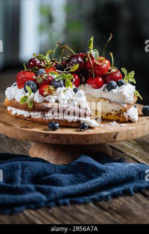 Frischer, saisonaler Kuchen mit Frühlingsreifen Früchten wie Erdbeeren, Heidelbeeren und Kirschen. Auf einem eleganten blauen Teller auf einem rustikalen Holzbrett Stockfoto