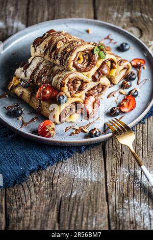 Crepes mit Schokoladenfüllung in Pyramidenform mit Erdbeeren der Saison, Kirschen und Blaubeeren auf einem rustikalen blauen Teller Stockfoto