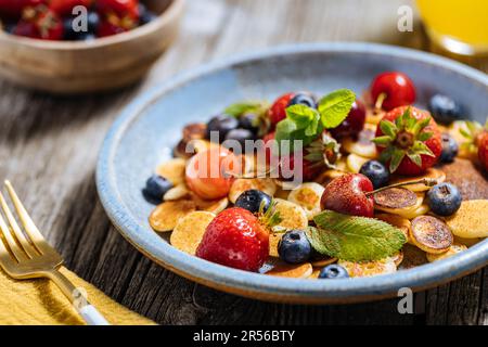 Kleine amerikanische Pfannkuchen mit Obst der Saison wie Erdbeeren, Heidelbeeren und Kirschen. Mit geschmolzener Schokolade getaucht, auf rustikalem Holz Stockfoto