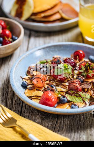 Kleine amerikanische Pfannkuchen mit Obst der Saison wie Erdbeeren, Heidelbeeren und Kirschen. Mit geschmolzener Schokolade getaucht, auf rustikalem Holz Stockfoto