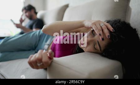 Besorgte junge Frau, die auf der Couch liegt und unter emotionalen Schmerzen leidet. Verstörte weibliche Person in 30s fühlt sich vom Freund getrennt in der Hintergrund-ST Stockfoto