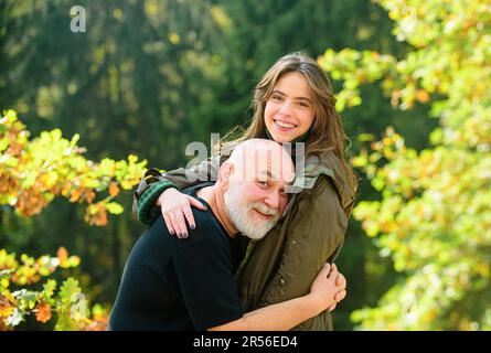 Glücklicher älterer Vater und Tochter genießen zarten Herbstmoment, lächelnd. Erwachsene Tochter umarmt reifen Mann von hinten, zwei Generationen Spaß haben Stockfoto