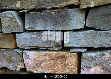 Eine alte, trockene Steinschiefergartwand. Die Steine sind gestapelt. Die Farbe ist hauptsächlich grau Stockfoto