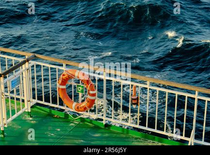 Ein orangefarbenes Rettungsboot auf dem Geländer einer Passagierfähre auf See. Großer Blickwinkel. Stockfoto