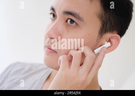 Nahaufnahme des Teilgesichts eines jungen Asiaten, der weiße, echte, kabellose Stereokopfhörer hört. Konzentrier dich auf die Augen. Stockfoto