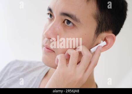 Nahaufnahme des Teilgesichts eines jungen Asiaten, der weiße, echte, kabellose Stereokopfhörer hört. Konzentrier dich auf die Augen. Stockfoto