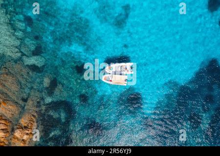 Blick aus der Vogelperspektive auf wunderschöne kleine Boote im blauen Meer bei Sonnenuntergang Stockfoto