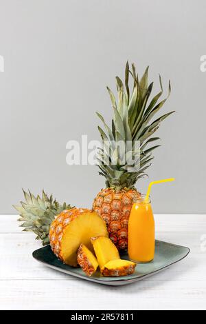 Scheiben saftiger Ananas und ein frischer, gesunder Smoothie in einer Glasflasche und ein Strohhalm auf einer grünen Platte auf Holzhintergrund. Gesund, Entgiftung und Dieta Stockfoto