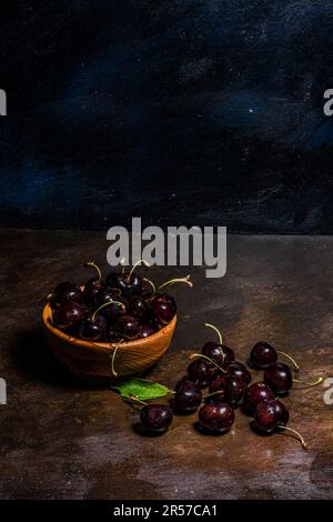 Handgedrehte Holzschüssel mit frisch vom Baum geernteten Kirschpflücken. Rustikale Atmosphäre. Vom Autor handgemalte Hintergründe. Stockfoto