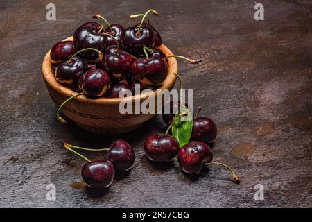 Handgedrehte Holzschüssel mit frisch vom Baum geernteten Kirschpflücken. Rustikale Atmosphäre. Vom Autor handgemalte Hintergründe. Stockfoto