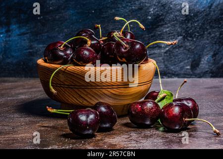 Handgedrehte Holzschüssel mit frisch vom Baum geernteten Kirschpflücken. Rustikale Atmosphäre. Vom Autor handgemalte Hintergründe. Stockfoto