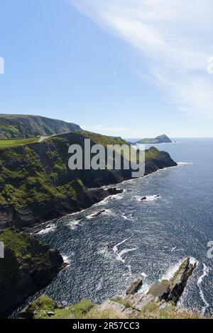 Halten Sie die atemberaubende Schönheit der vertikalen Klippen Irlands fest, die in ein atemberaubendes Licht getaucht sind, vor dem Hintergrund eines leuchtend blauen Himmels und des glitzernden Meeres. Stockfoto