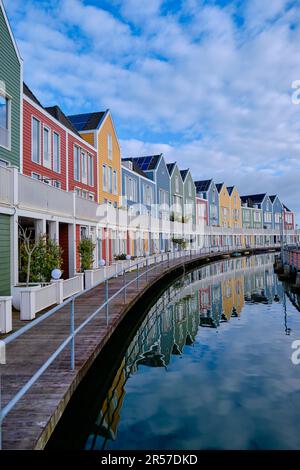 Houten, Niederlande - April 25 2023. Eine Reihe farbenfroher Holzhäuser am See. Spiegelt sich im Wasser des Sees de Rietplas wider. Schwindende Perspektive. Stockfoto