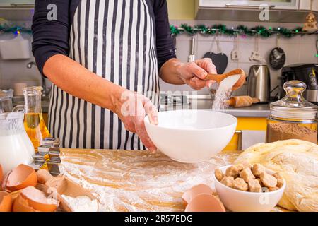 Eine Frau in einer gestreiften Kochschürze, die die Zutaten mit einem Löffel umrührt, während sie Weihnachten Lebkekse kocht, Nahaufnahme Stockfoto