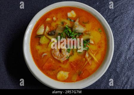 Tom Yum Meeresfrüchtesuppe in einer weißen Schüssel auf dunklem Hintergrund. Flach liegend, über Kopf Stockfoto