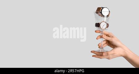 Frauenhände mit Weinglas und stilvollen Armbanduhren auf hellem Hintergrund mit Platz für Text Stockfoto