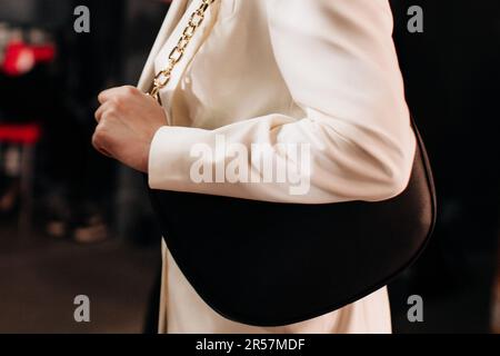 Modische Details: Weiße, elegante Jacke und schwarze Lederhandtasche mit goldener Kette. Style, Design von Damenbekleidung und Accessoires. Stockfoto