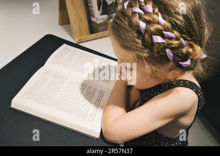 Ein süßes, kleines, weißes Mädchen, das ein Buch am Schreibtisch liest Stockfoto