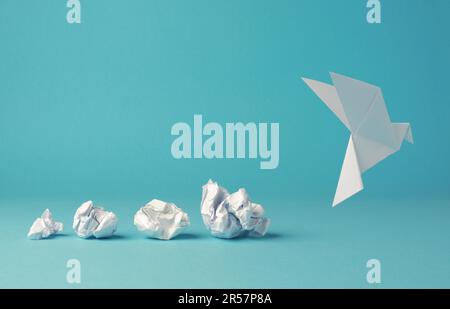 Zerknitterte Papierkugeln mit Origami-Papiertaube, Friedens-, Freiheit- oder Chancenkonzept auf blauem Hintergrund Stockfoto