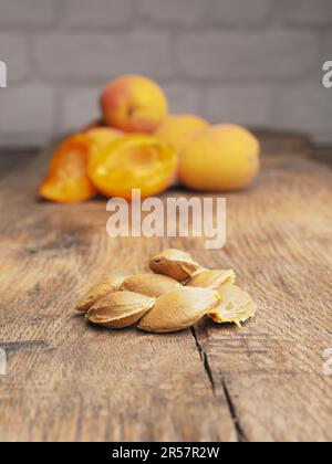 Nahaufnahme von Aprikosengruben auf einem rustikalen Gartentisch, Landwirtschaftskonzept, frische Bio-Pfirsiche im Hintergrund Stockfoto