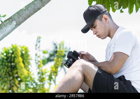 Junger Latino-Mann, der im Außendienst sitzt und sich die Inhalte ansieht, die er mit seiner Social-Media-Kamera aufgenommen hat. Stockfoto