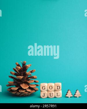 Kleine Holzblöcke mit der Aufschrift God Jul, Scandinavian Merry Christmas, türkisfarbener Hintergrund, minimalistische Weihnachtsdekoration aus Holz Stockfoto