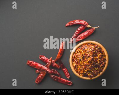 Chiliflocken in der Holzschüssel und getrocknete Paprika auf schwarzem Paprika-Hintergrund. Getrocknete und zerkleinerte Früchte von Capsicum frutescens, die als heiße Gewürze verwendet werden, und Stockfoto