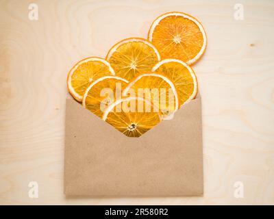 Öko-Bio hausgemachte getrocknete Orangenscheiben, Chips, in einem handwerklich hergestellten Umschlag auf Holzhintergrund. Getrocknete, knusprige Fruchtscheiben. Ein Haufen sonnengetrockneter Haufen Stockfoto