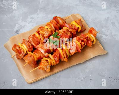 Ungekochte marinierte und geriebene Chiken- oder truthahn-Shish-Kebabs auf Spießen mit Zwiebeln, Pfeffer und Tomaten zum Grillen oder Grillen. Rohes Fleisch in einer Marinade Stockfoto